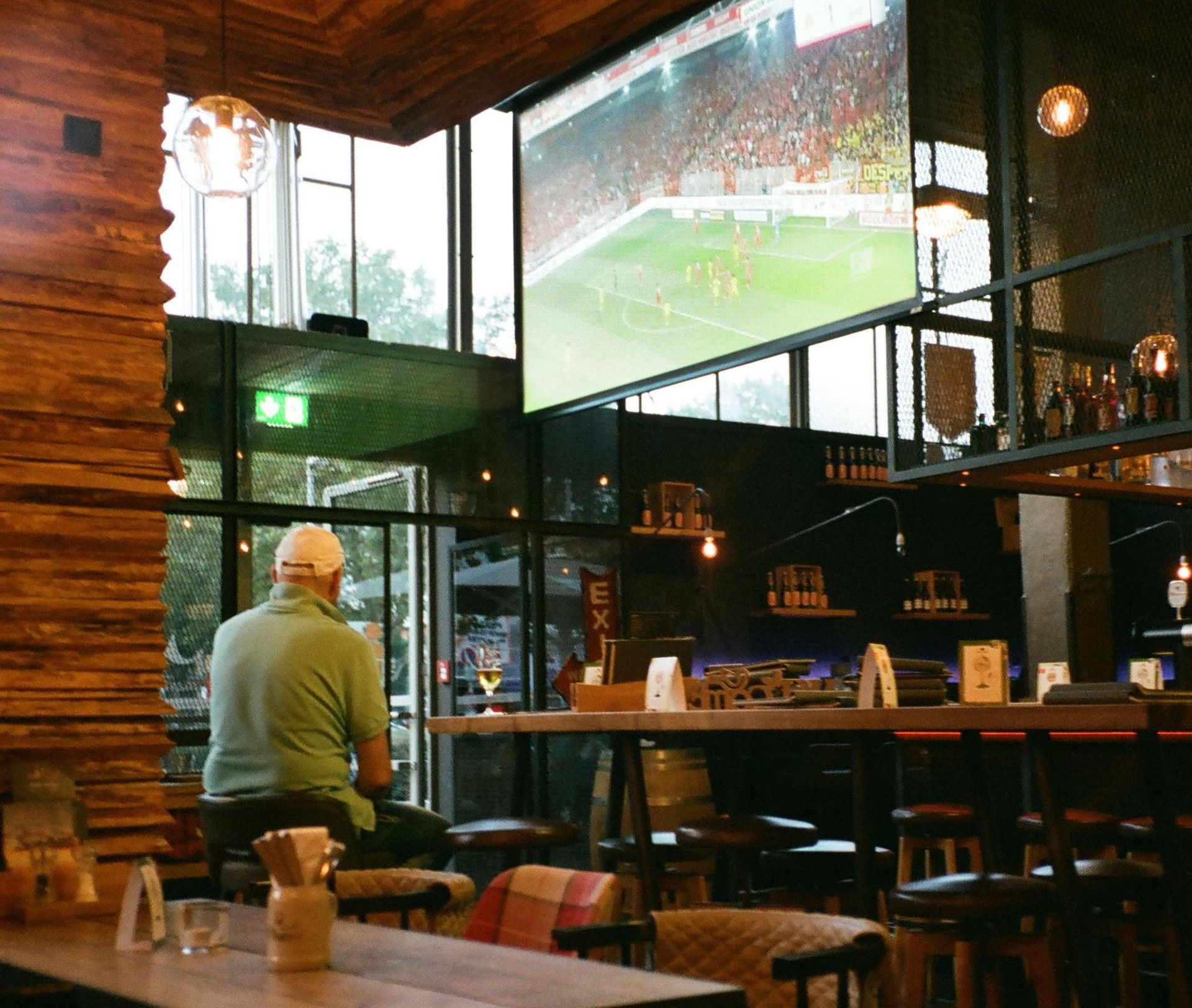 Ein Mann schaut sich in einer Bar ein Fußballspiel auf einer Großleinwand an; Holzinterieur, Fenster.