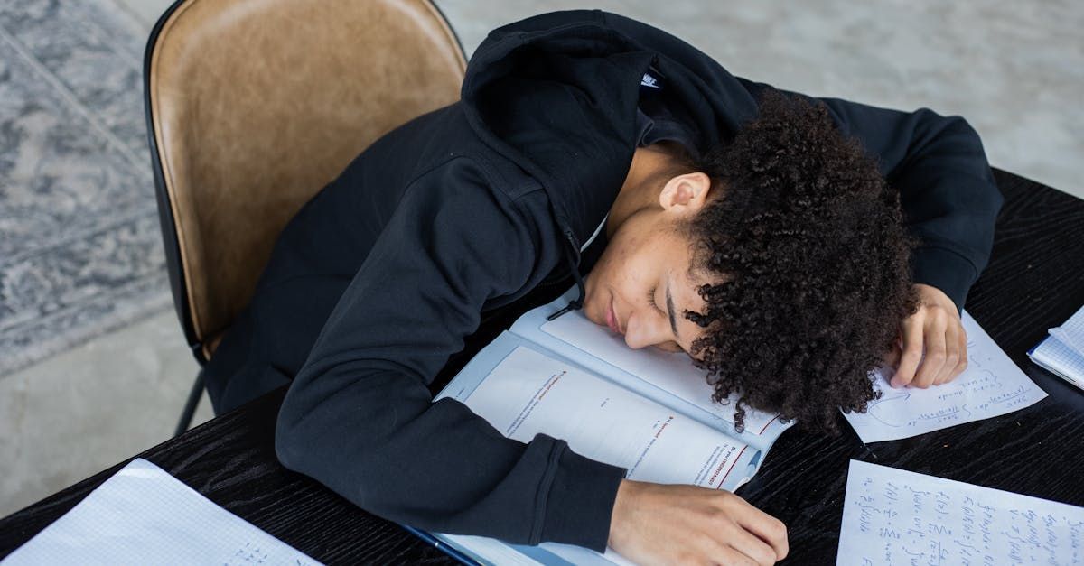 Prüflinge, die im schriftlichen Teil des ersten Staatsexamens durchgefallen sind, nennt das JPA Hamm intern Eine Person schläft an einem Schreibtisch mit Papieren und Notizbüchern, den Kopf auf verschränkten Armen.