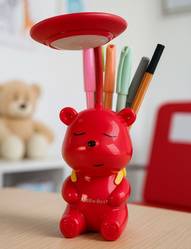 Red bear-shaped desk lamp holding pens, with a teddy bear in the background.