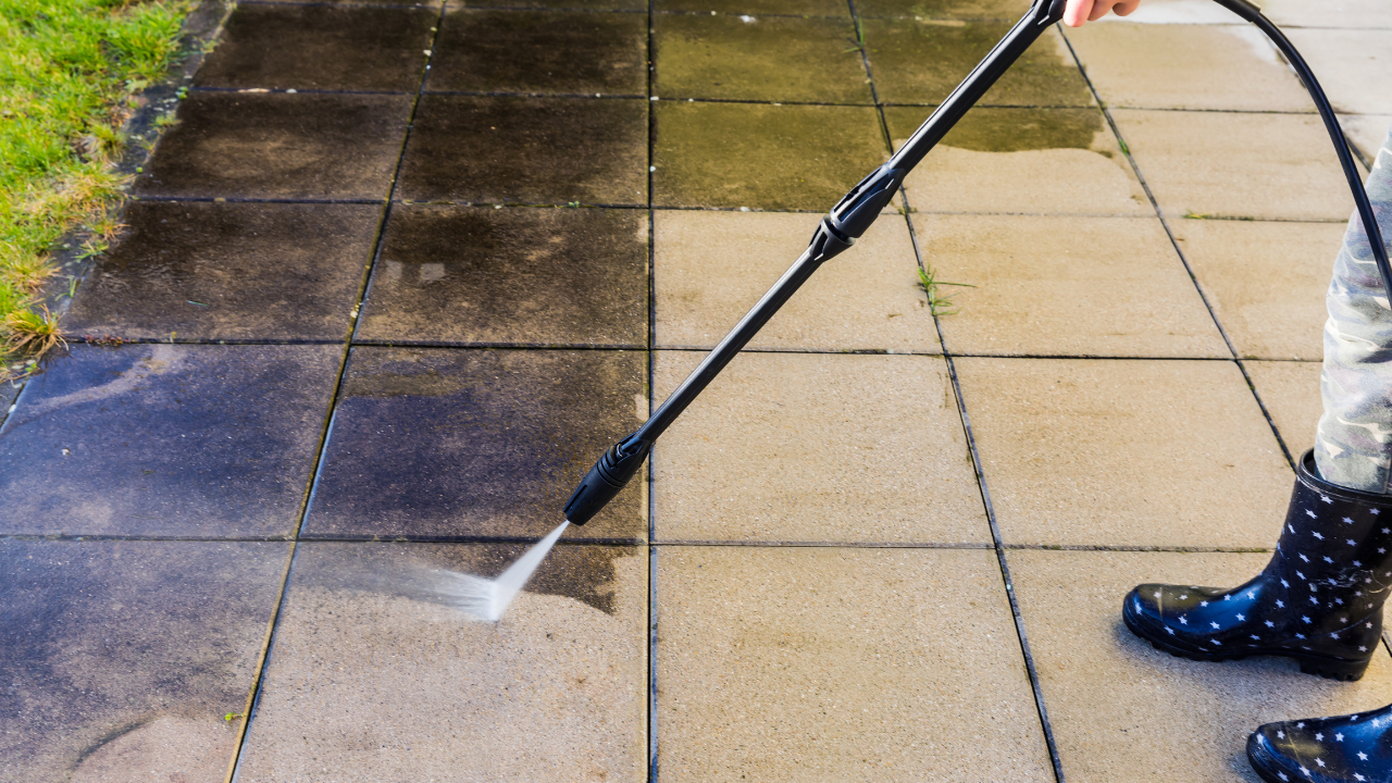 Person pressure-washing a tiled patio, spraying dirty water off the surface.