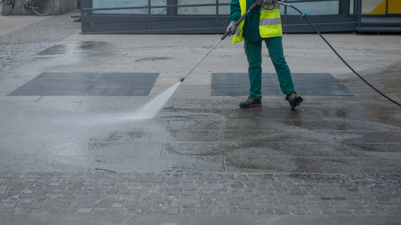 Worker pressure-washing a wet concrete surface outside a building