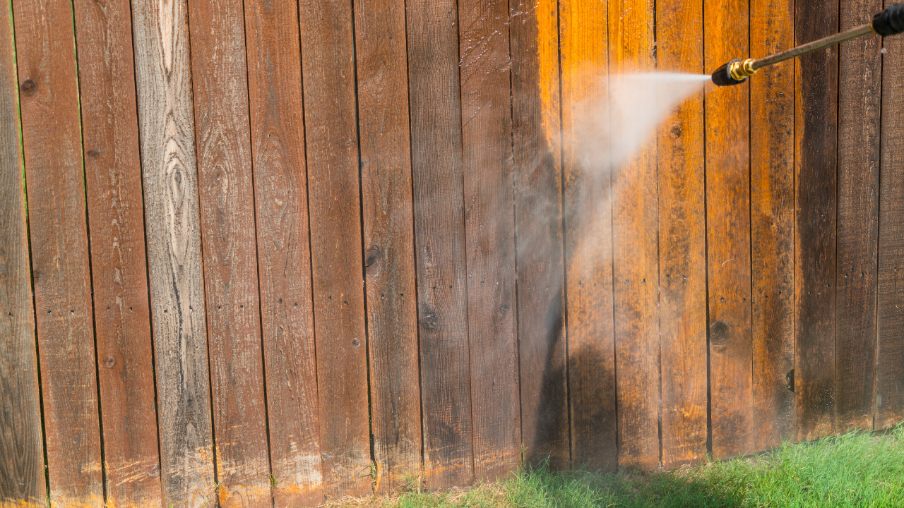 Water spraying against a weathered wooden fence in a yard