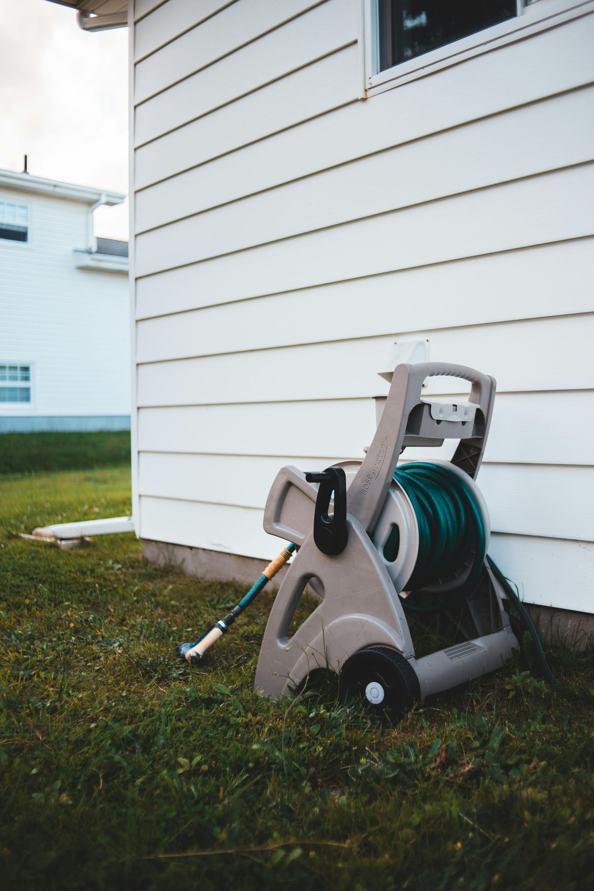 Garden hose reel cart beside a white house, with green hose and blue-handled nozzle on grass