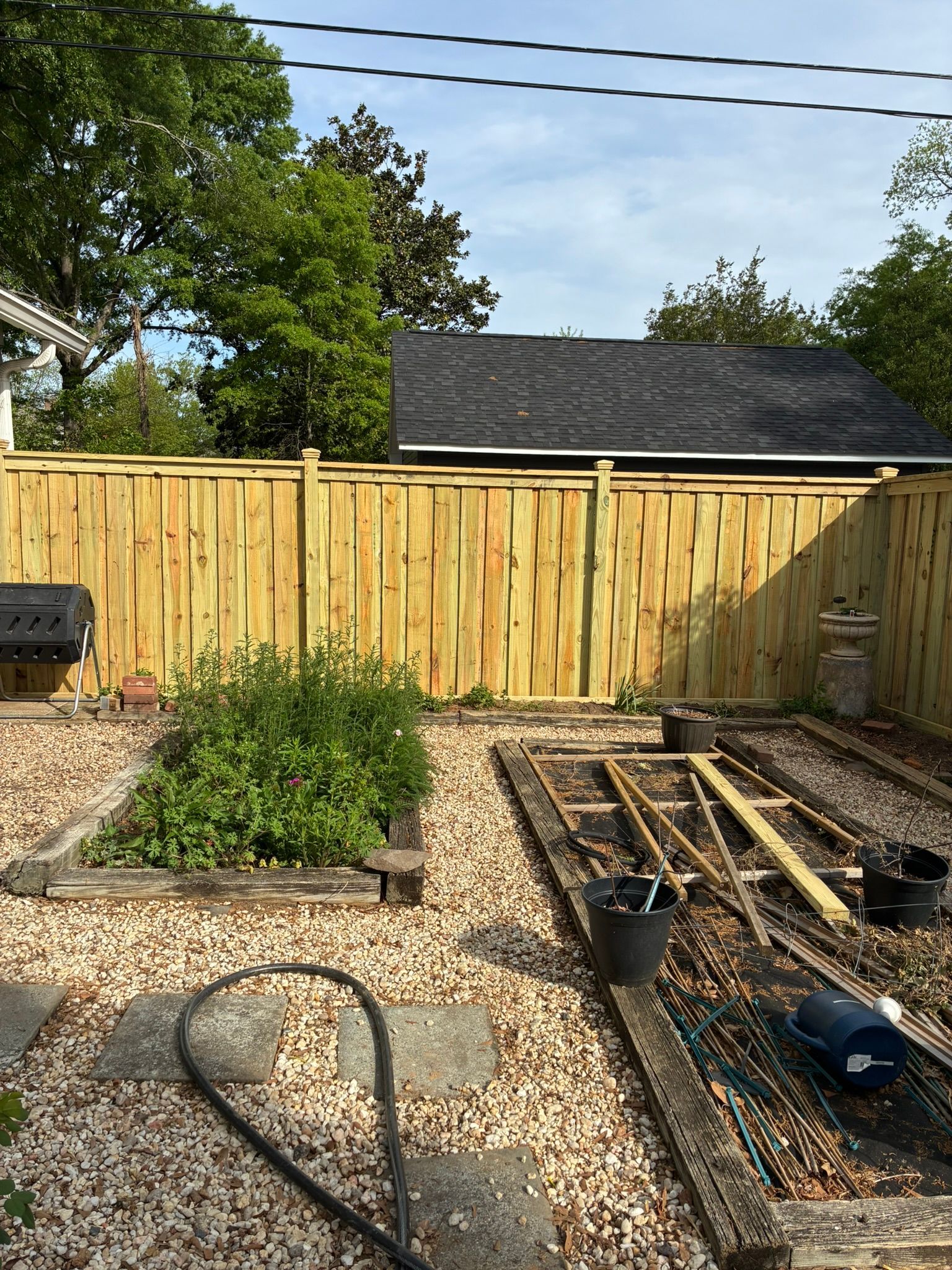 Wooden fence along a grassy yard, with a small building visible in the background against a blue sky.