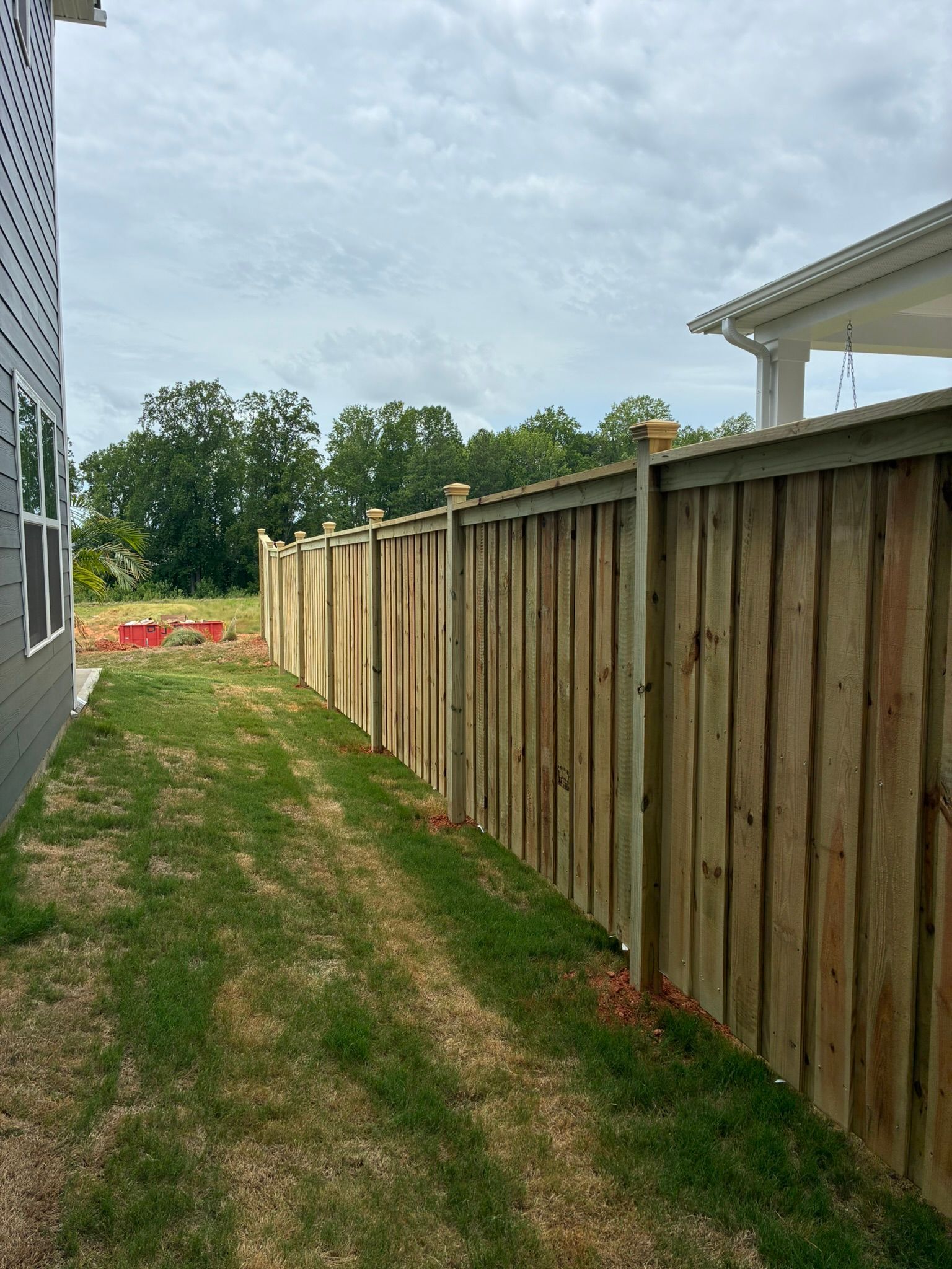 Wooden fence curving along a grassy yard under a blue sky with clouds, small shed in the distance.