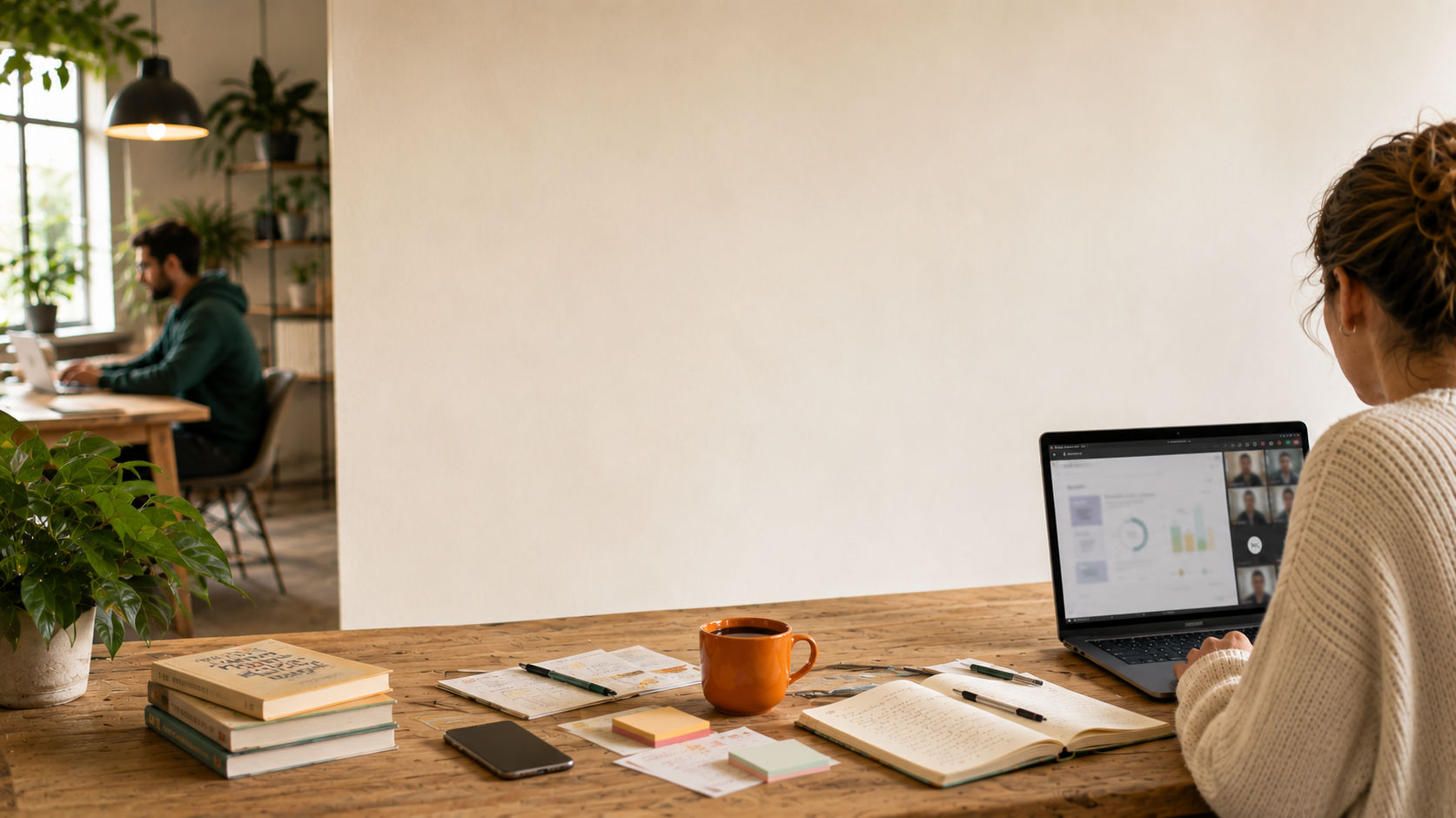 Laptop mit Online-Meeting, Notizbuch, Smartphone und orangefarbener Kaffeetasse 