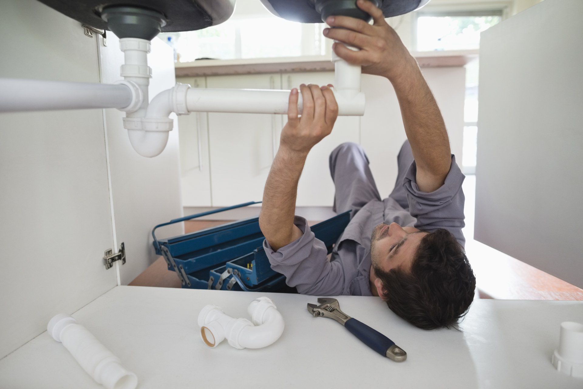 Man Plumber Repairing Pipe Under Sink — Somers Point, NJ — McBride & Company Plumbing, Heating, Air Conditioning Man Plumber Repairing Pipe Under Sink — Somers Point, NJ — McBride & Company Plumbing, Heating, Air Conditioning