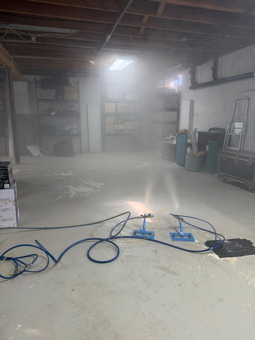 Dusty basement workshop with exposed ceiling, shelves, tools, and blue cords on the floor