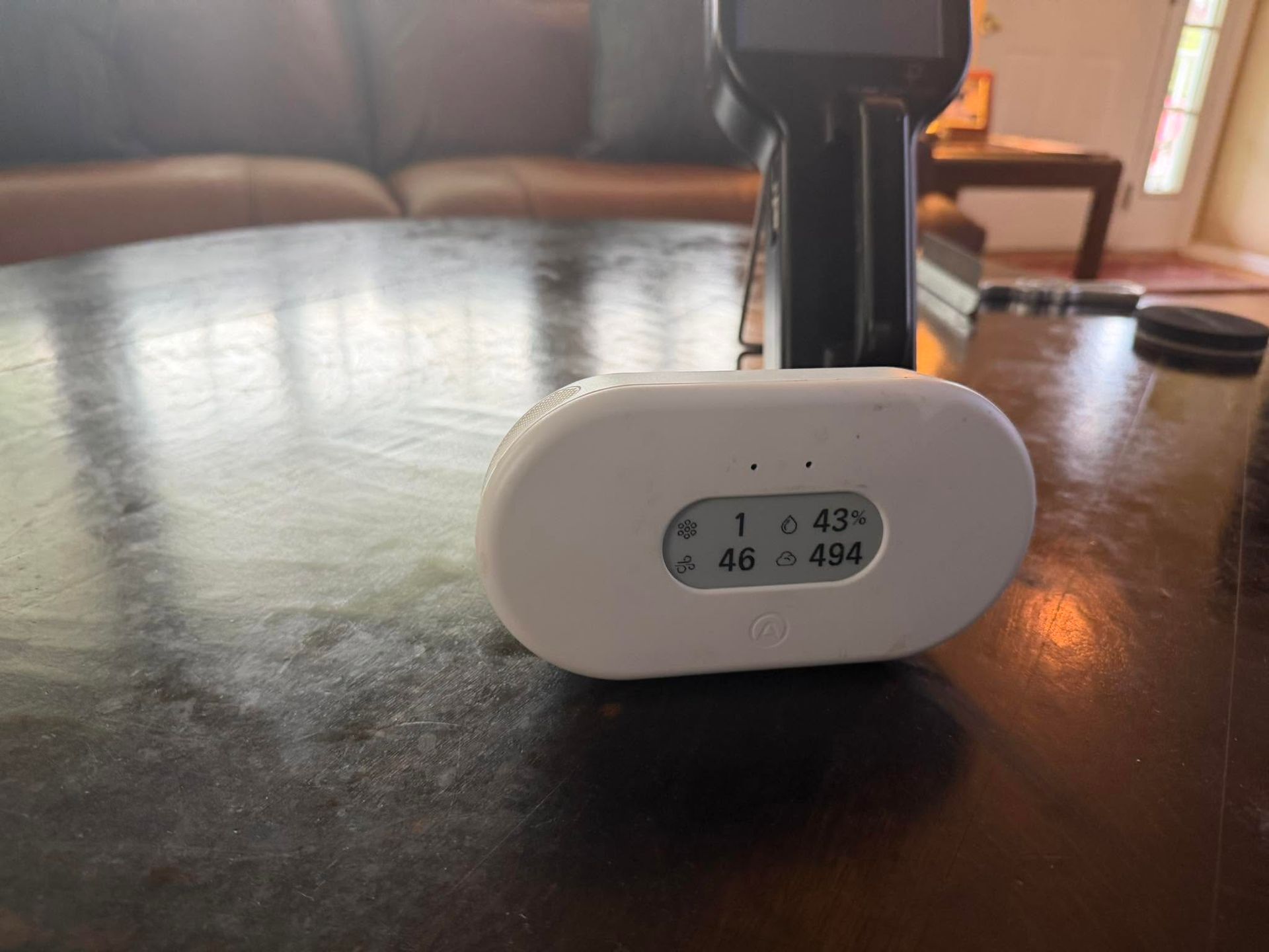 White digital thermometer/hygrometer on a dark table, showing indoor temperature and humidity readings.
