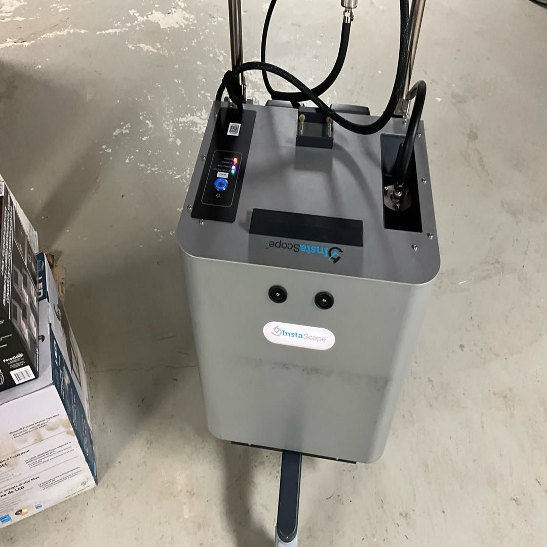 Gray hospital machine with hoses on a concrete floor beside a box in a utility room
