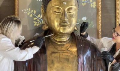 Two women repairing a Buddha statue with paint brushes