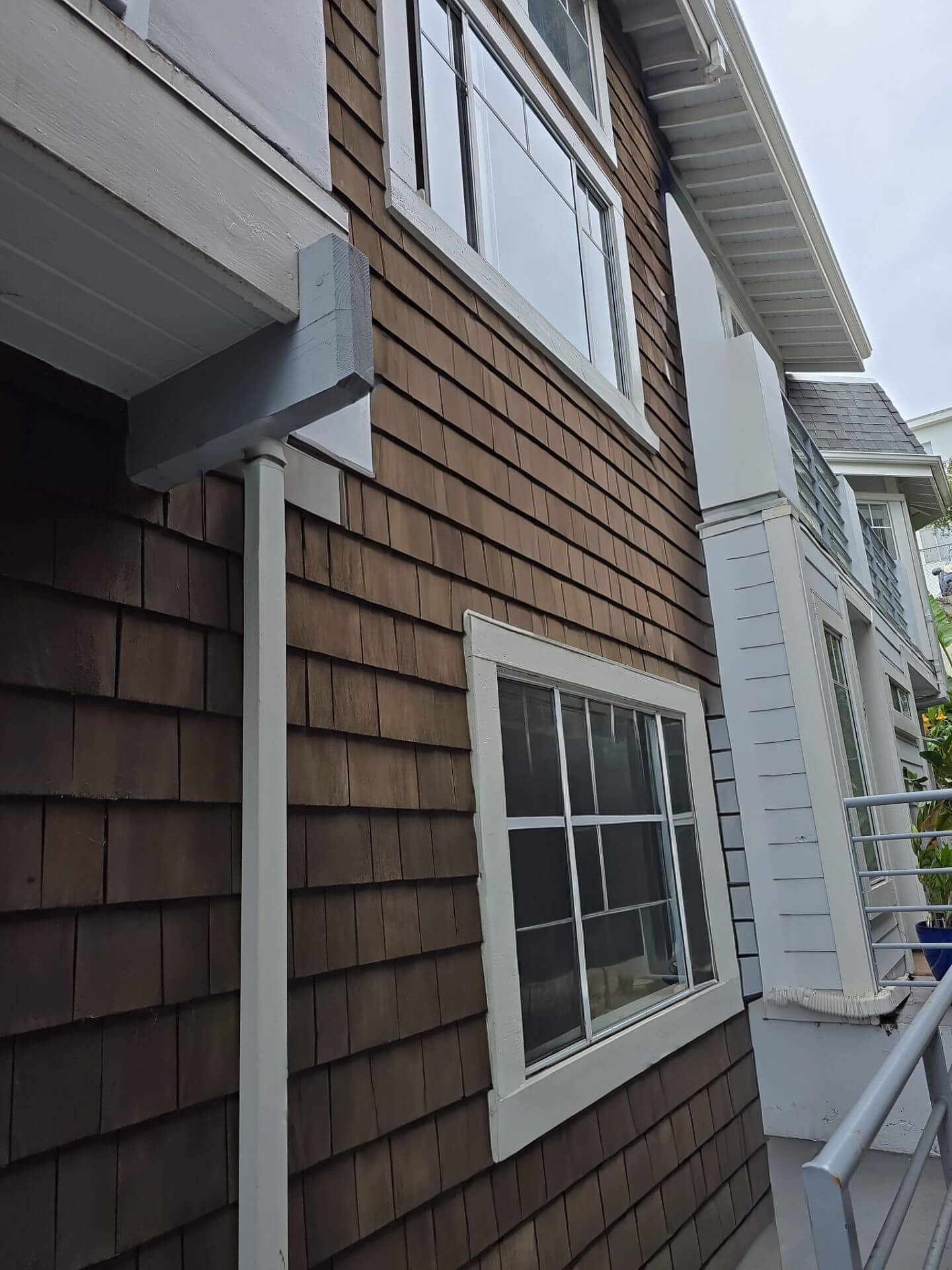 A low-angle view of a building exterior with brown wood shingles, white window frames, and a white vertical downspout.