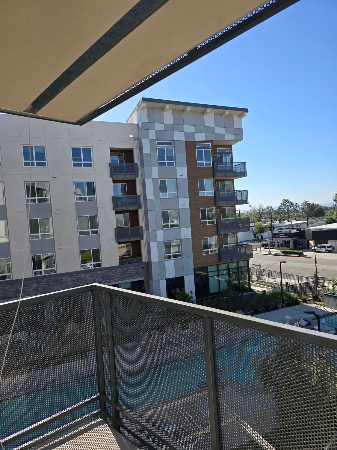 A view from a balcony overlooking a multistory apartment building with a checkered facade and a ground-level pool.