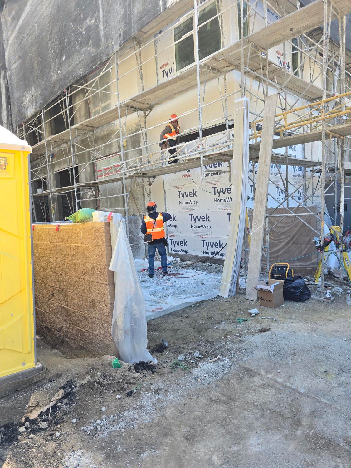 Construction workers in safety gear work on a building exterior surrounded by scaffolding and materials.