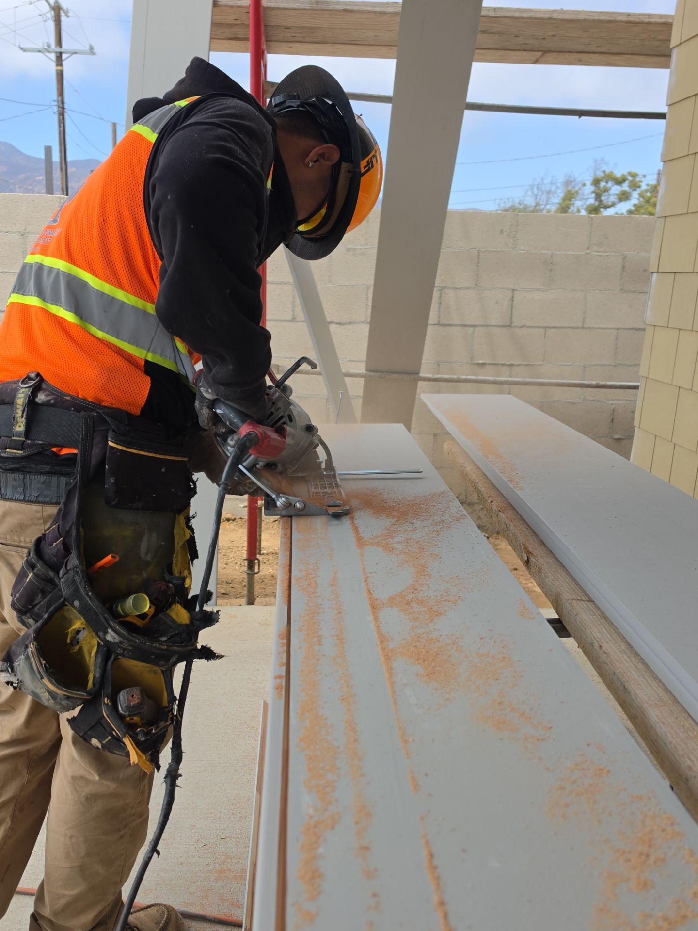 Worker in safety vest cutting a large white panel on a construction site with a power saw