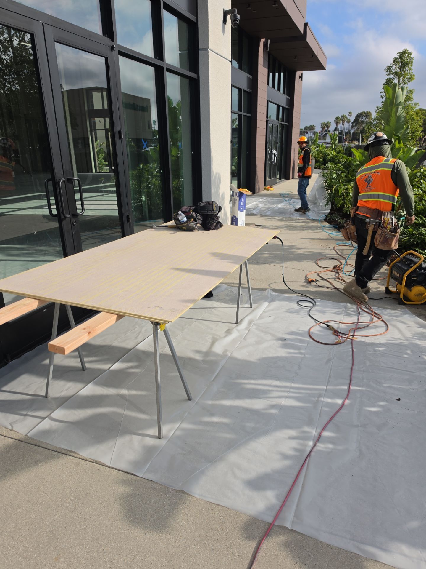 Construction workers setting up a temporary work area beside a modern glass building.