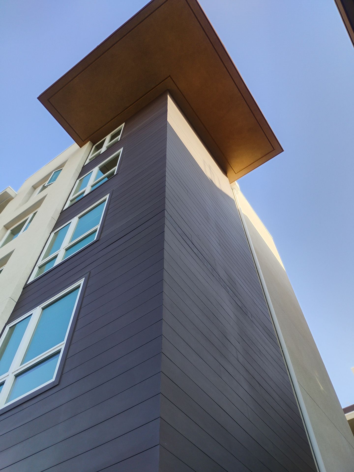 Low-angle view of a modern apartment building with a wood roof overhang against a blue sky