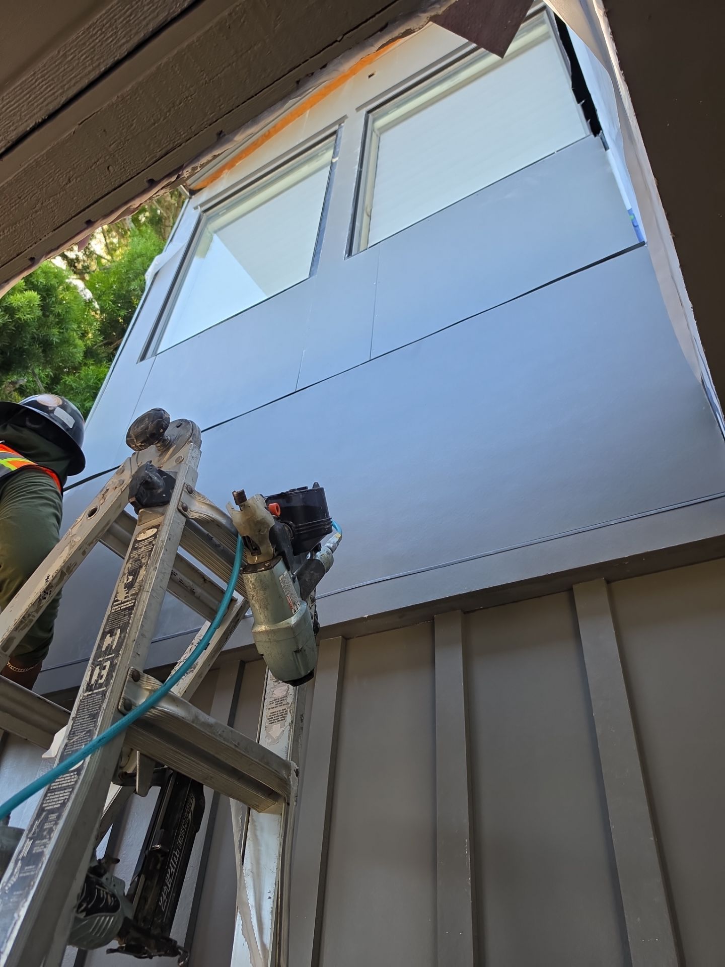 Worker painting the exterior of a house with a ladder and spray equipment