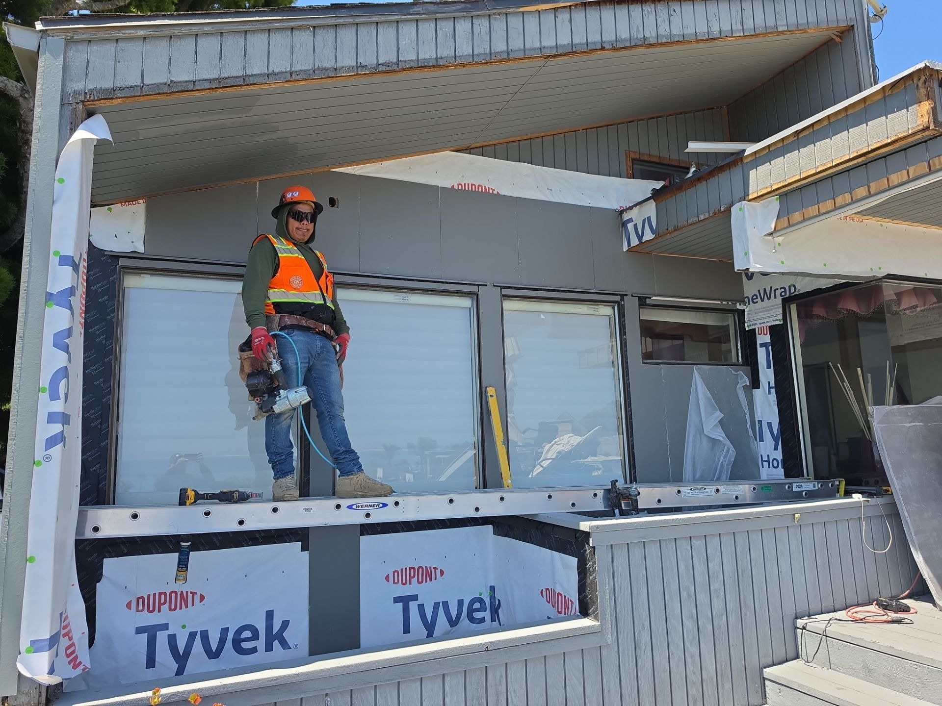 Worker standing on a front porch during home construction, with Tyvek wrap and unfinished siding.