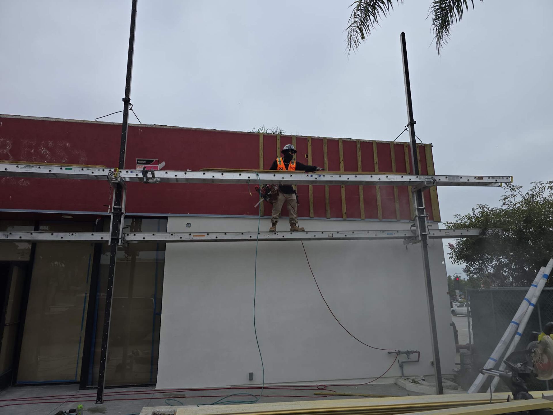 A worker in a safety vest stands on scaffolding while cutting into the exterior wall of a building.
