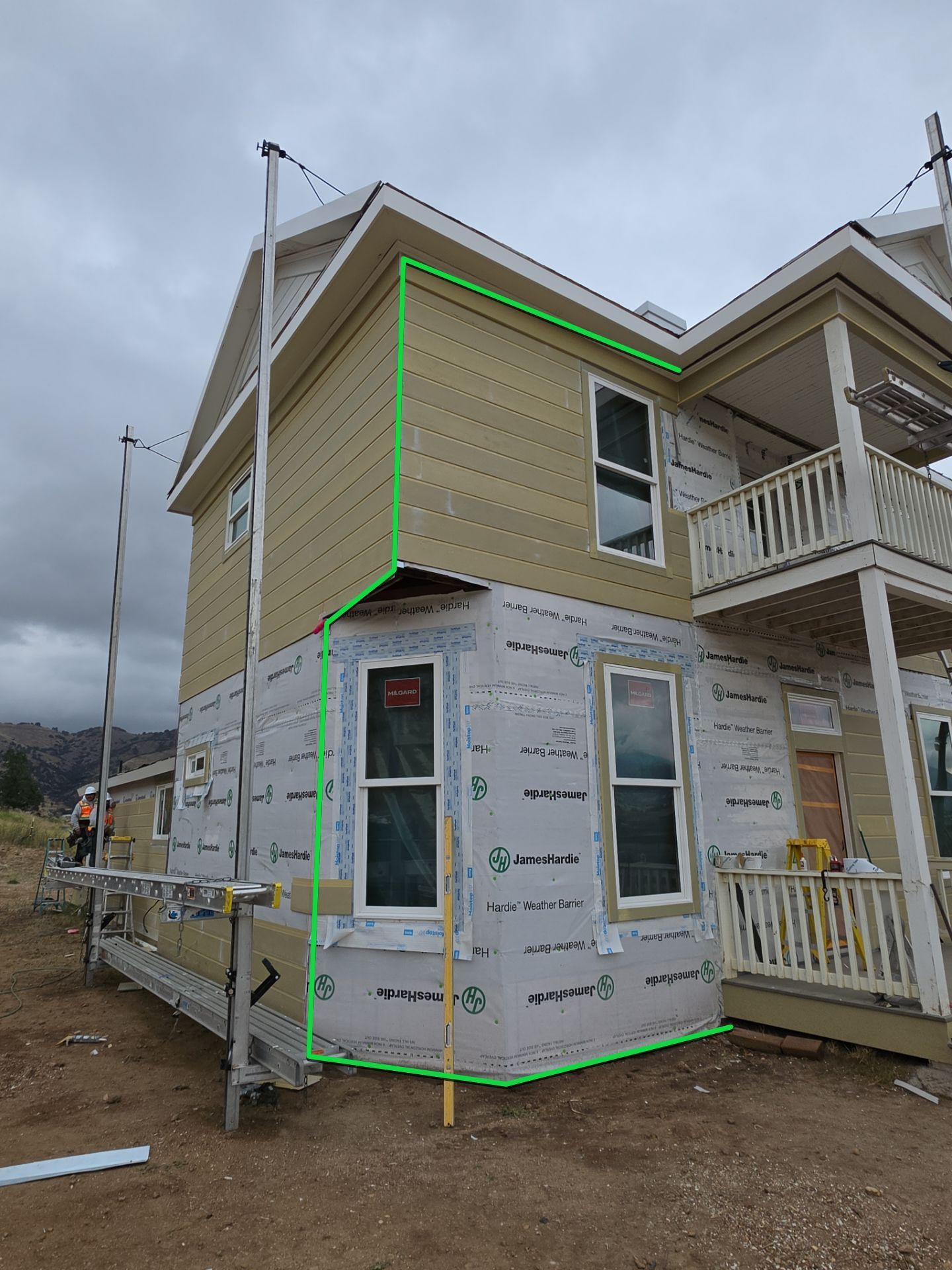 Partially built house with green trim and unfinished siding on a cloudy day