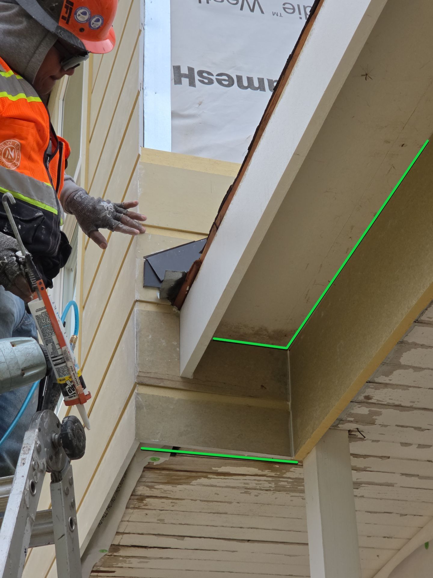 Construction worker measuring the underside of a roof overhang with green laser lines on a building exterior