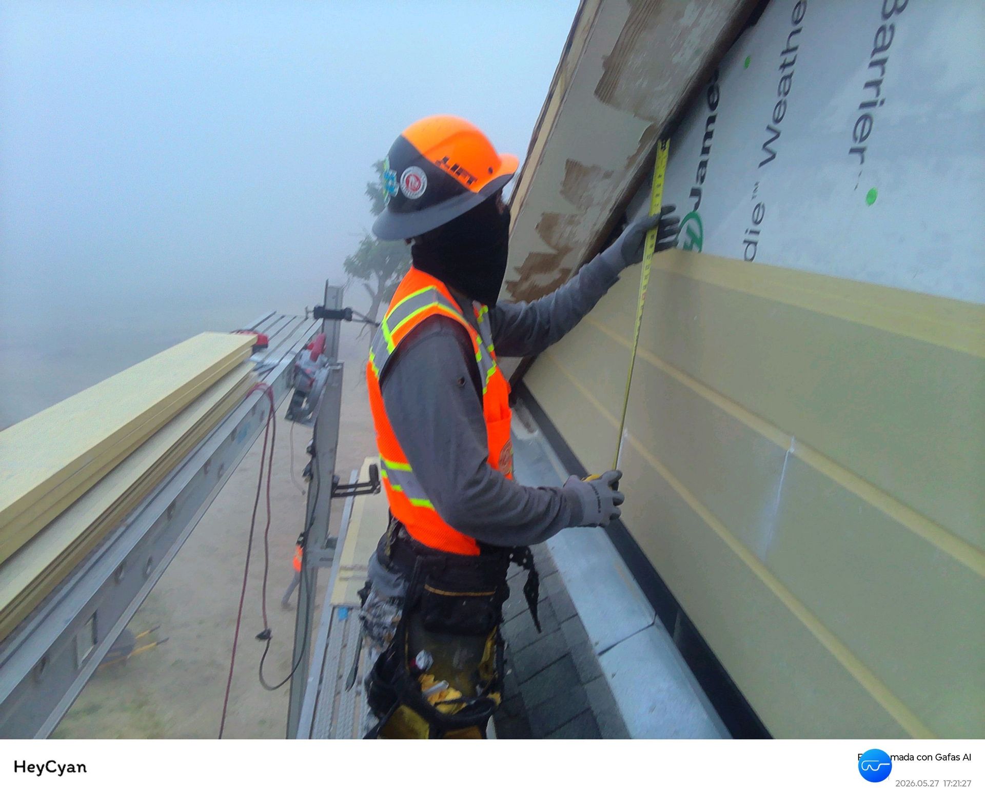 Worker in orange safety vest and hard hat securing insulation on a building exterior scaffold.