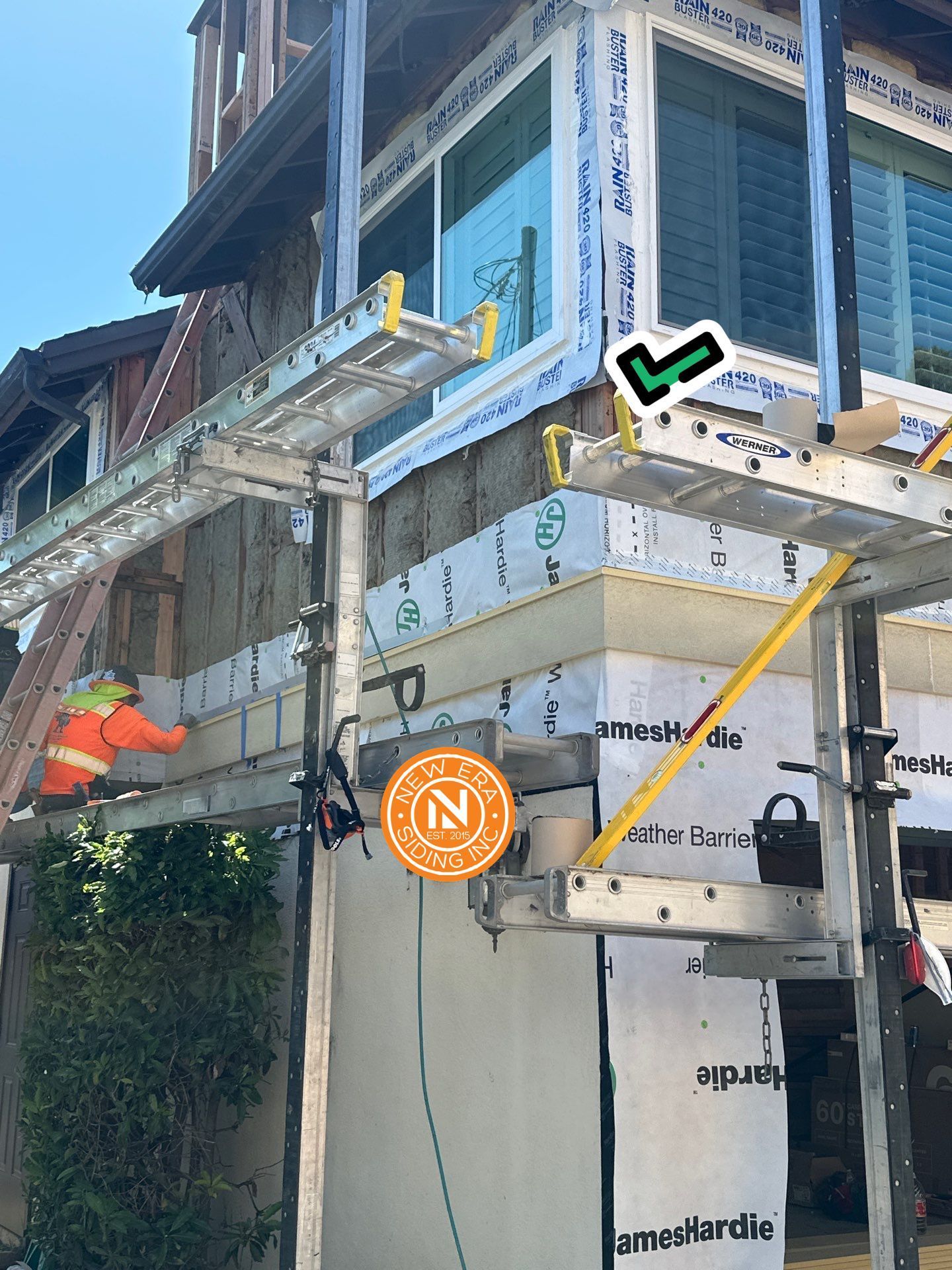Worker on scaffolding installing siding on a blue house exterior.