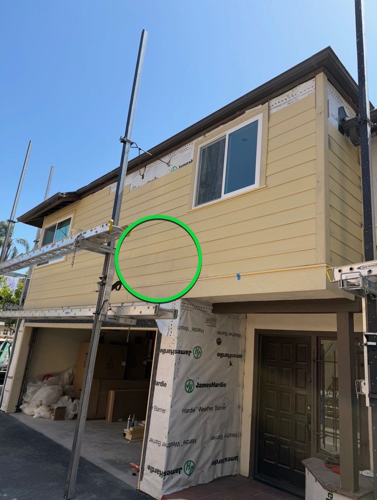 Yellow-sided house under renovation with scaffolding and a green circled area on the exterior wall