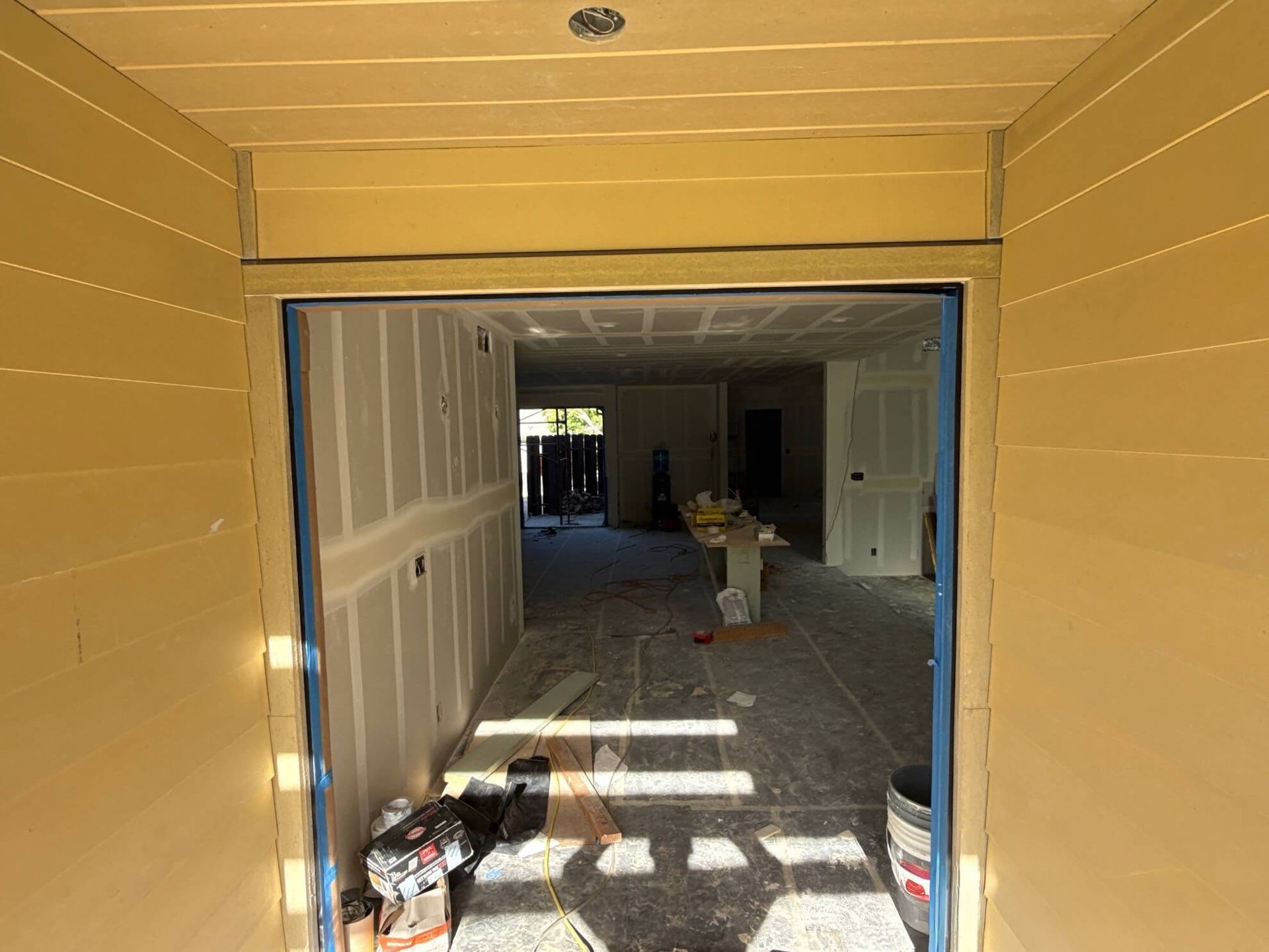 A view through a doorway into a room under renovation with drywall, construction debris, and light from an open exit.