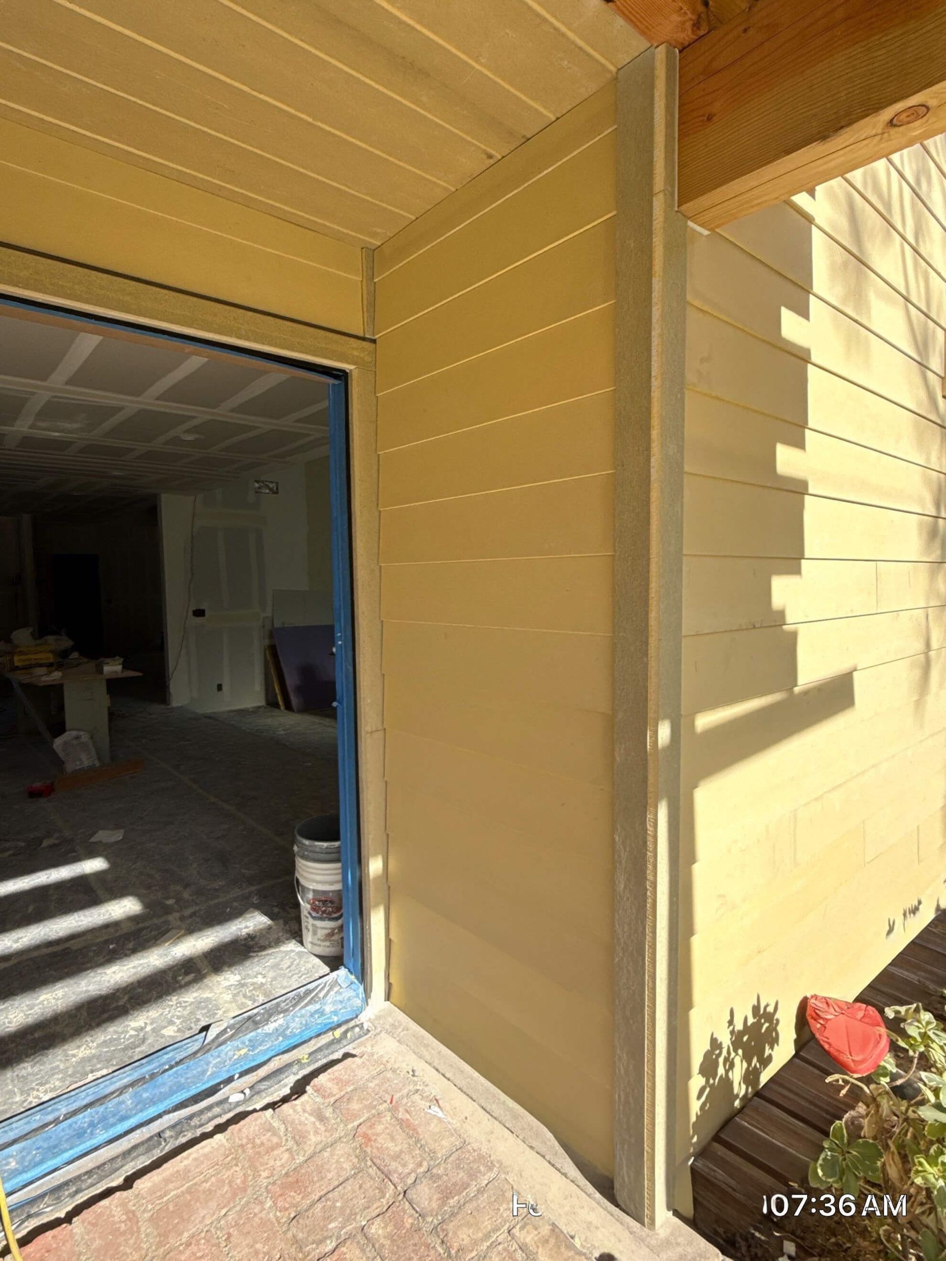 A doorway leading into a room under construction, with beige horizontal siding on the exterior wall and a brick walkway.