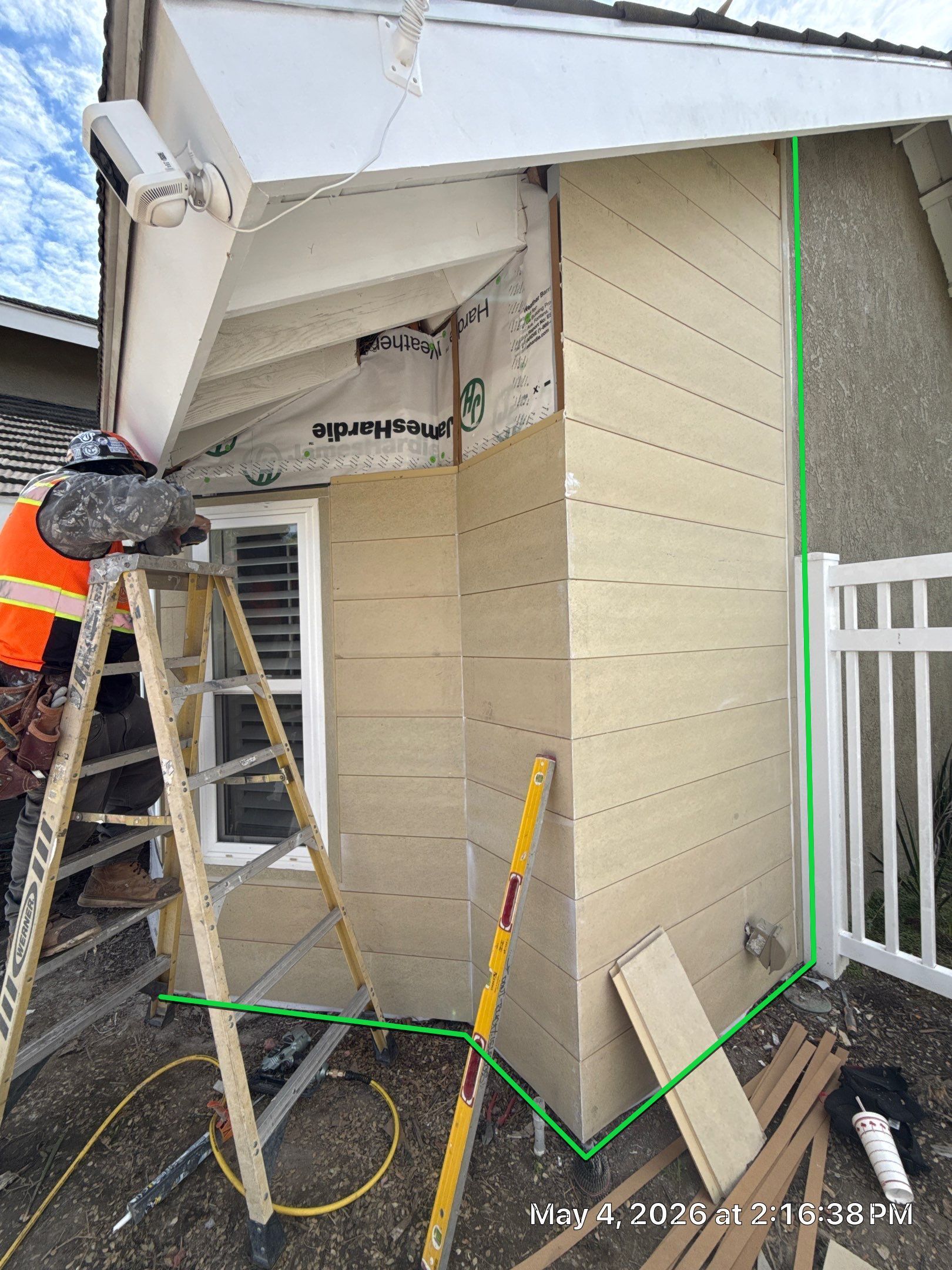 Worker on ladder repairing tan exterior wall and roof eave at a house corner
