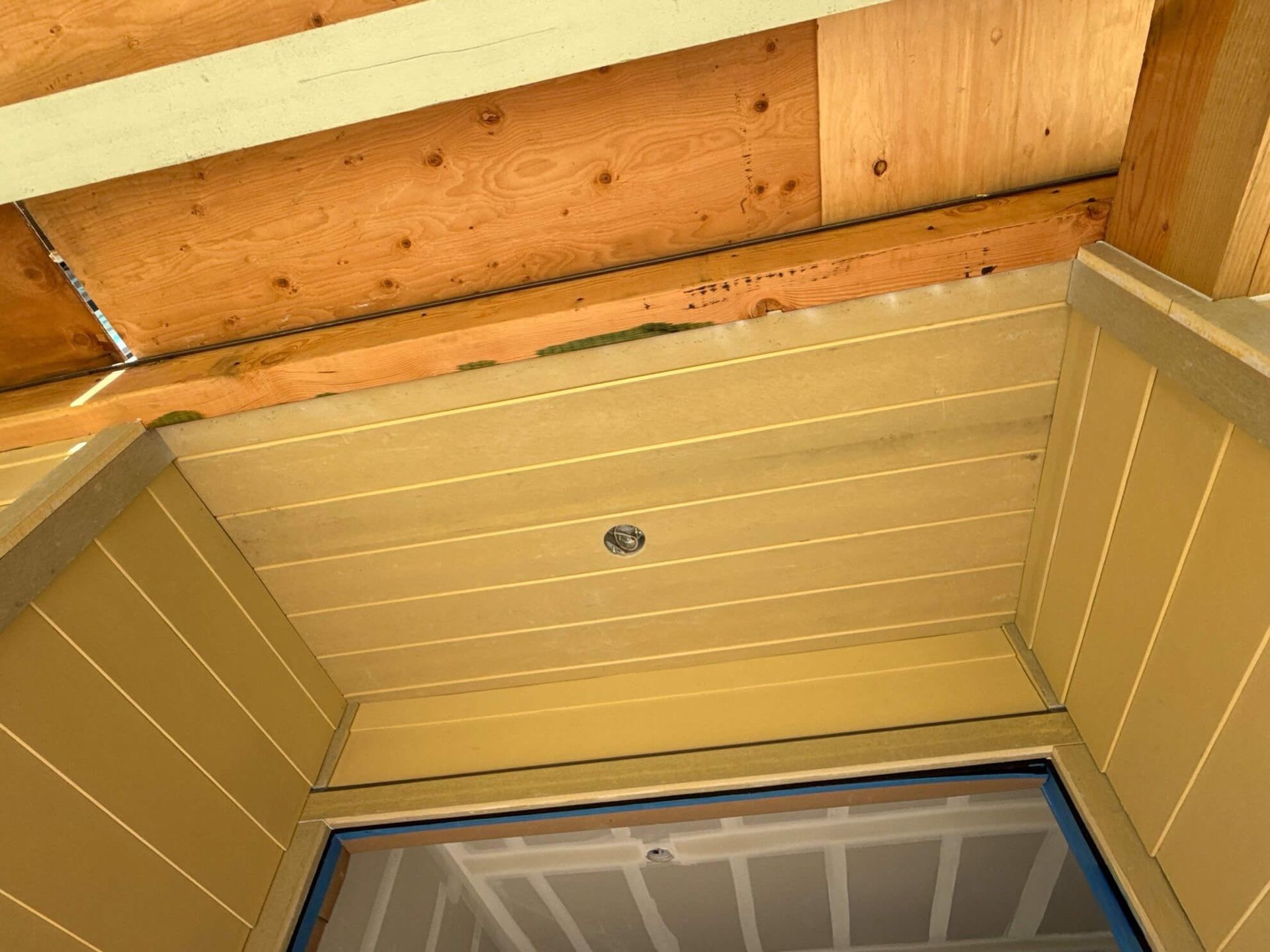 Low-angle view of a beige exterior ceiling soffit and wall paneling under a wood-framed roof overhang.