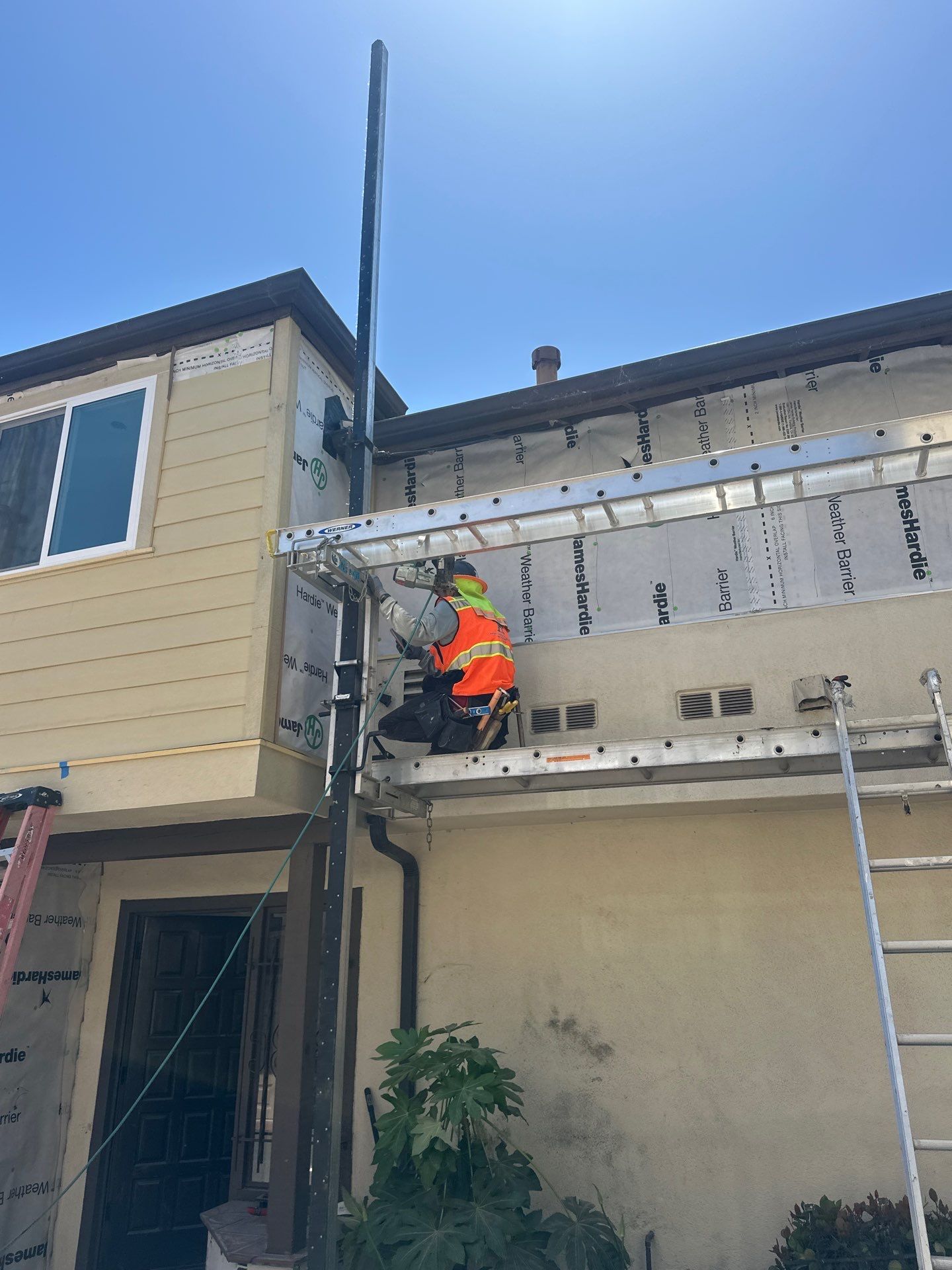 Worker in orange safety vest on a ladder repairing the exterior of a house roofline