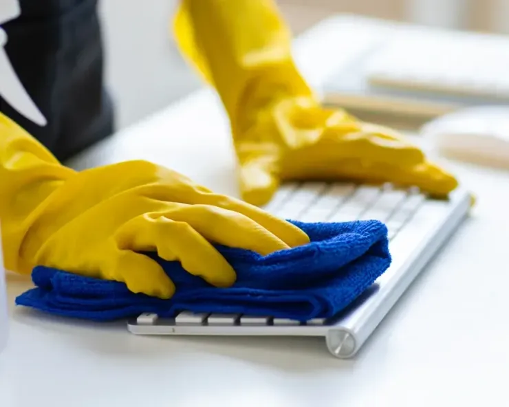 Yellow-gloved hands wiping a white keyboard with a blue cloth