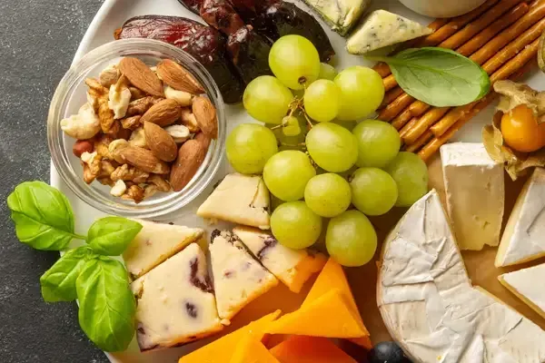 Cheese, grapes, crackers, nuts, and basil arranged on a wooden board