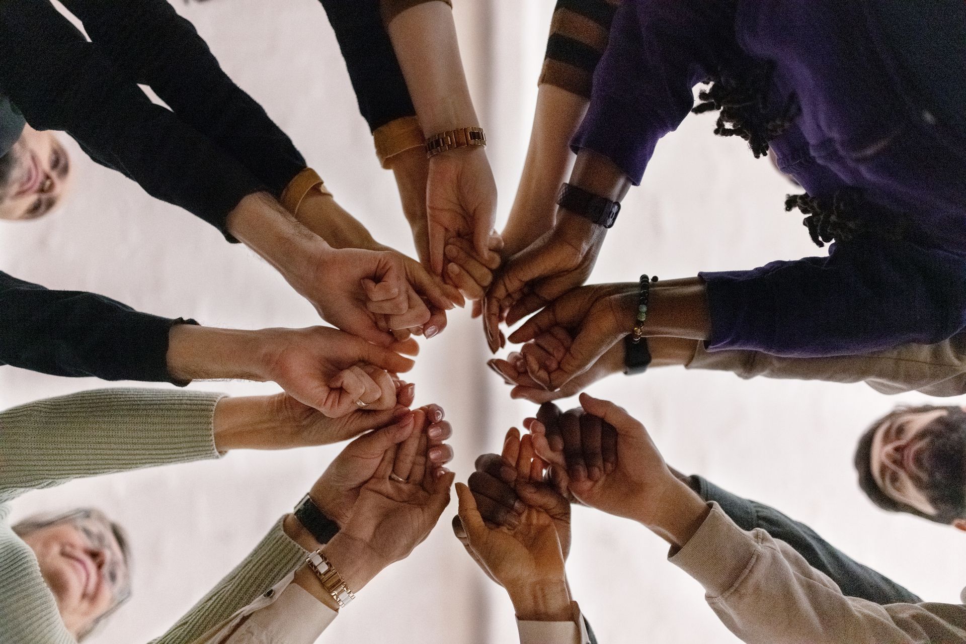 Persone che si tengono per mano in cerchio, viste dal basso, a simboleggiare unità e sostegno.