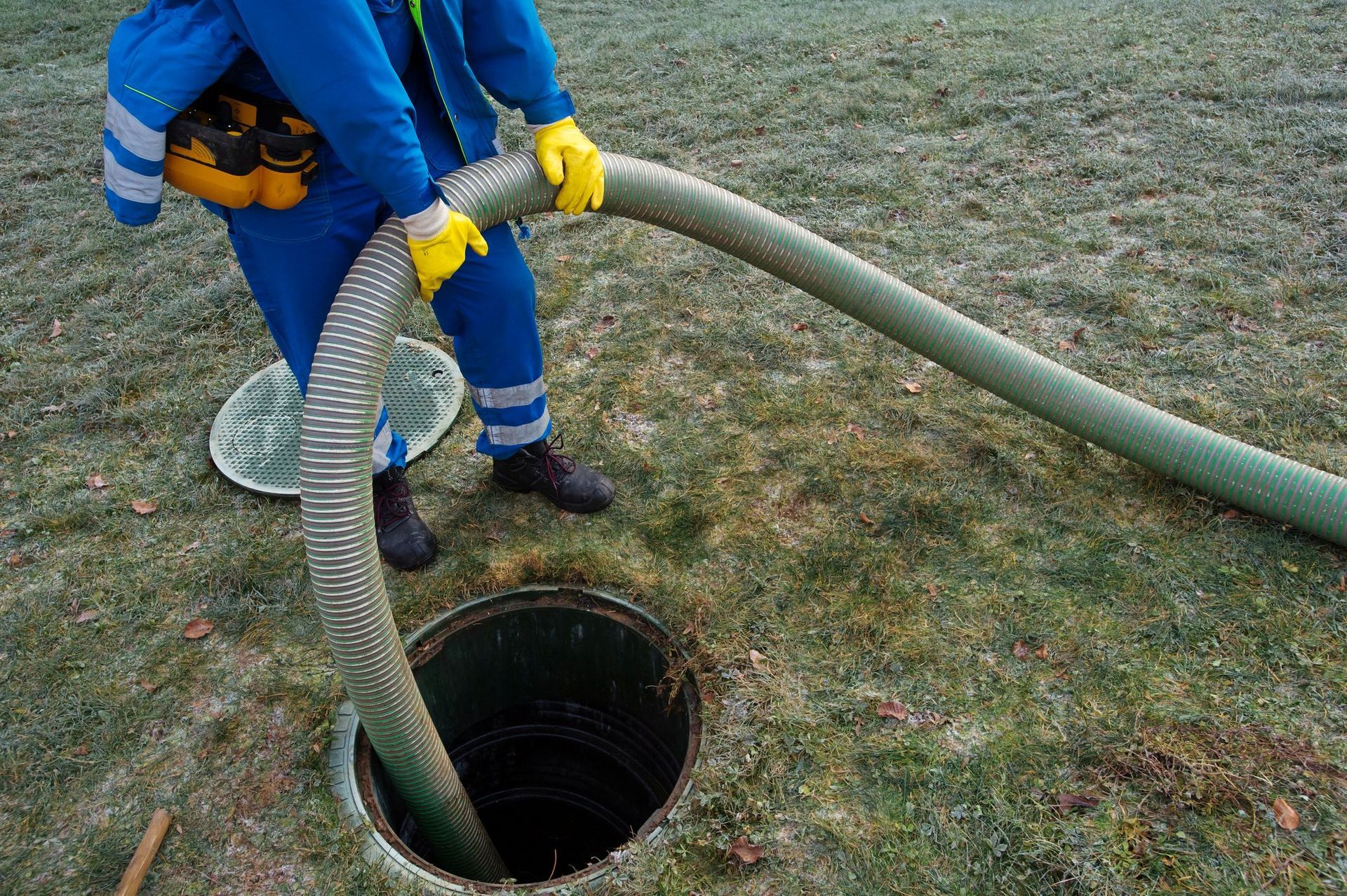 Worker pumping a septic tank with a large hose during outdoor residential septic system maintenance.