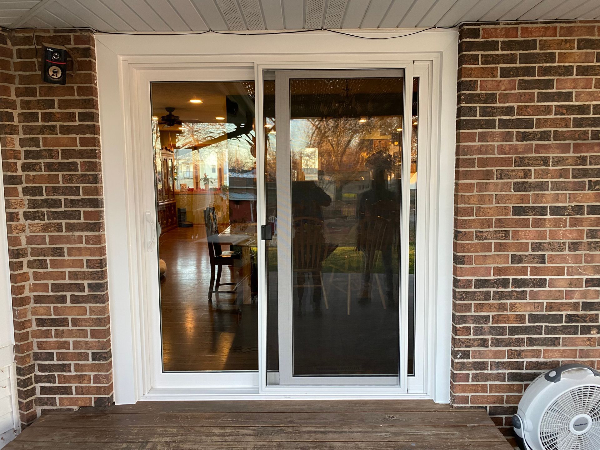 A white sliding glass door is on a brick wall next to a fan.