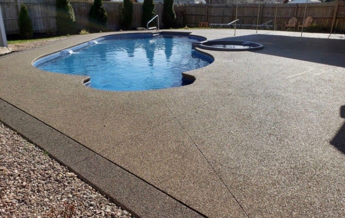 Backyard pool with a concrete deck and a stone border, shown on a sunny day