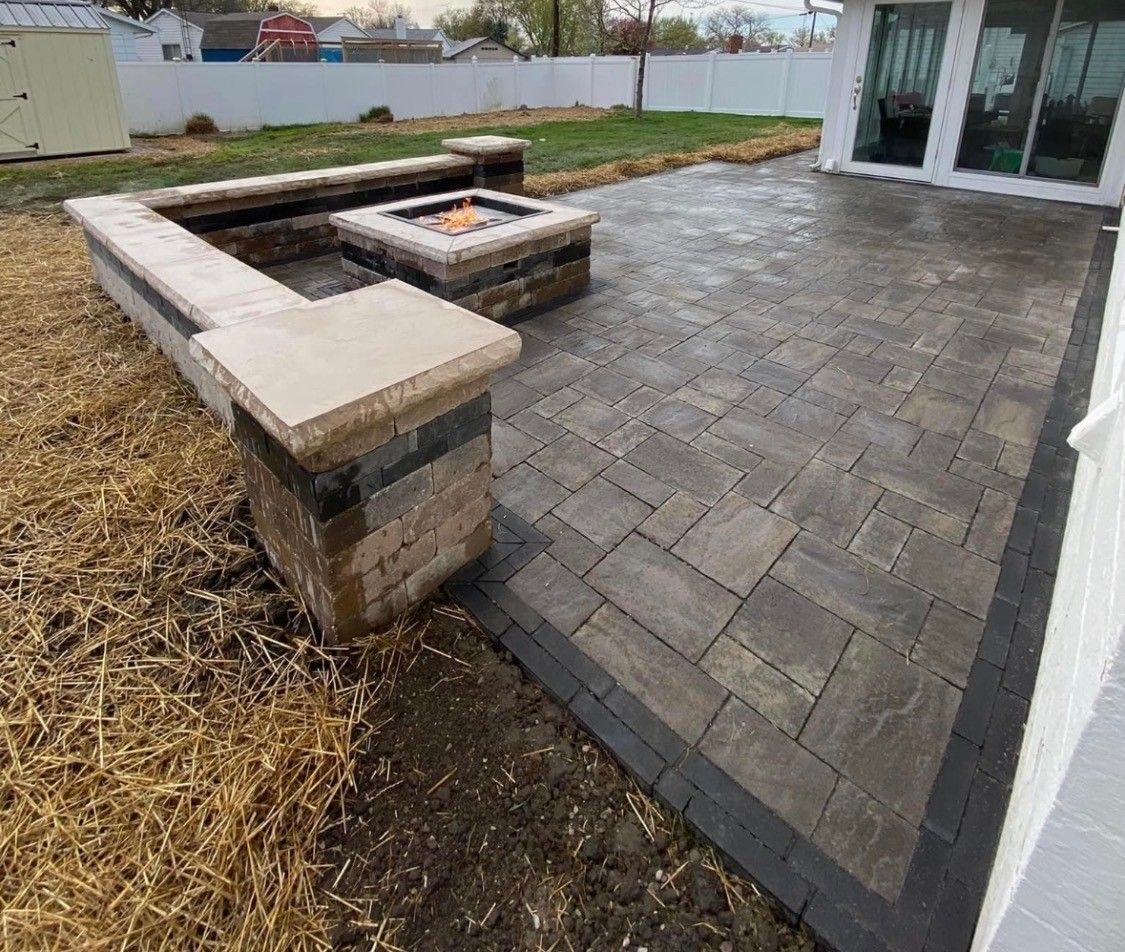 Outdoor stone patio with a built-in concrete and brick fire pit seating area next to a house