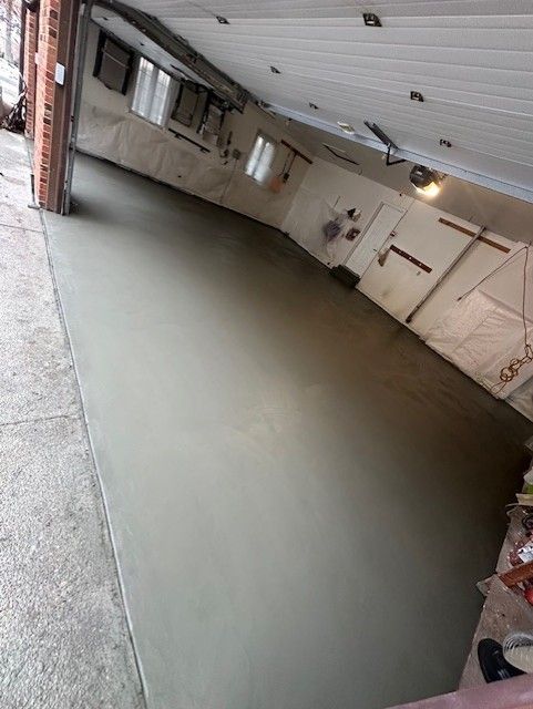 Tilted view of a large indoor concrete room with a freshly poured floor and white walls