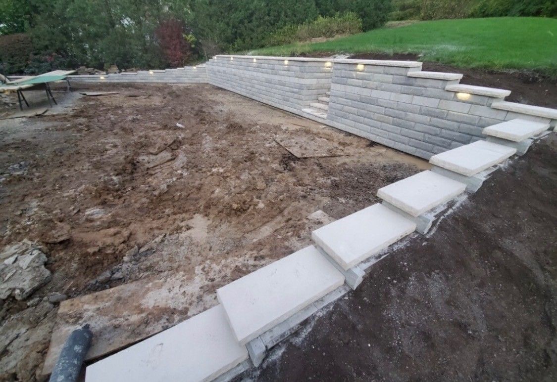 Terraced retaining wall steps around a dirt excavation site beside a grassy hillside