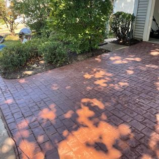 Brick patio beside a garden and house, with dappled sunlight and a walkway at the edge