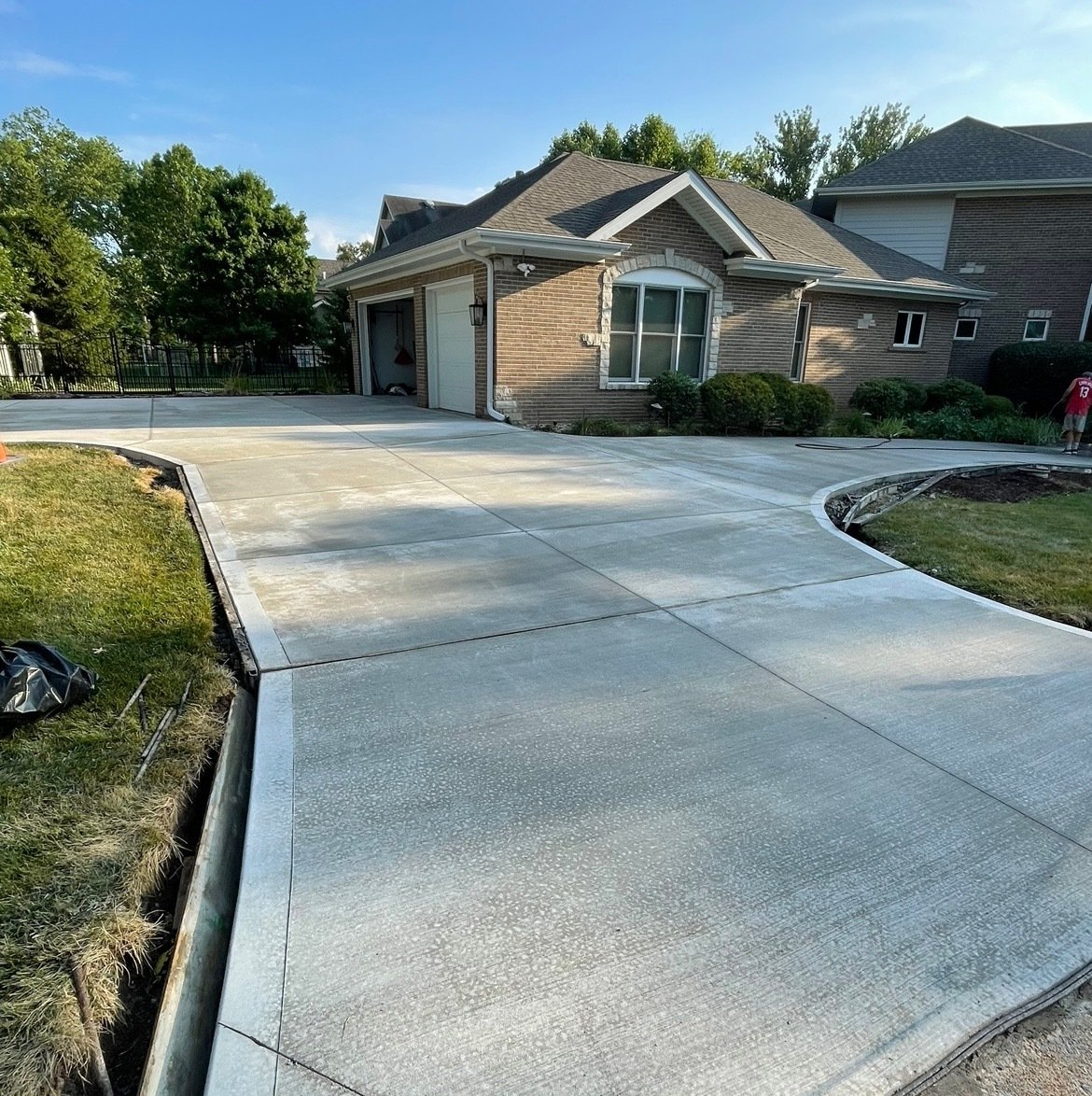 A concrete contractor with a yellow helmet is straightening and smoothing fresh driveway.