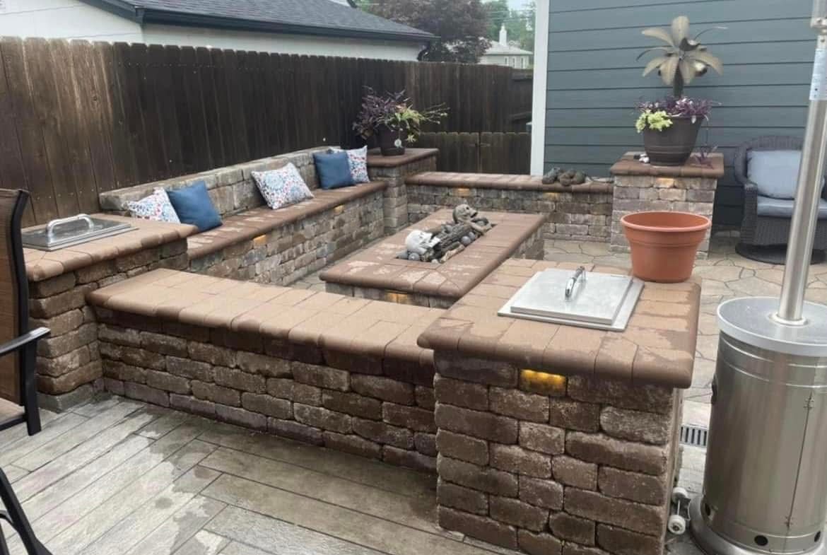 Backyard patio with brick seating, stone fire pit, potted plants, and a tall patio heater