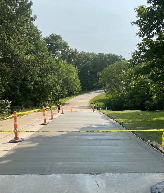 Closed park path under construction, with orange cones, yellow caution tape, and trees lining the road.