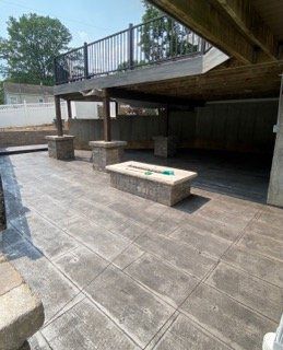 Covered outdoor patio with stone benches, tiled floor, and a railing above in a shaded backyard area