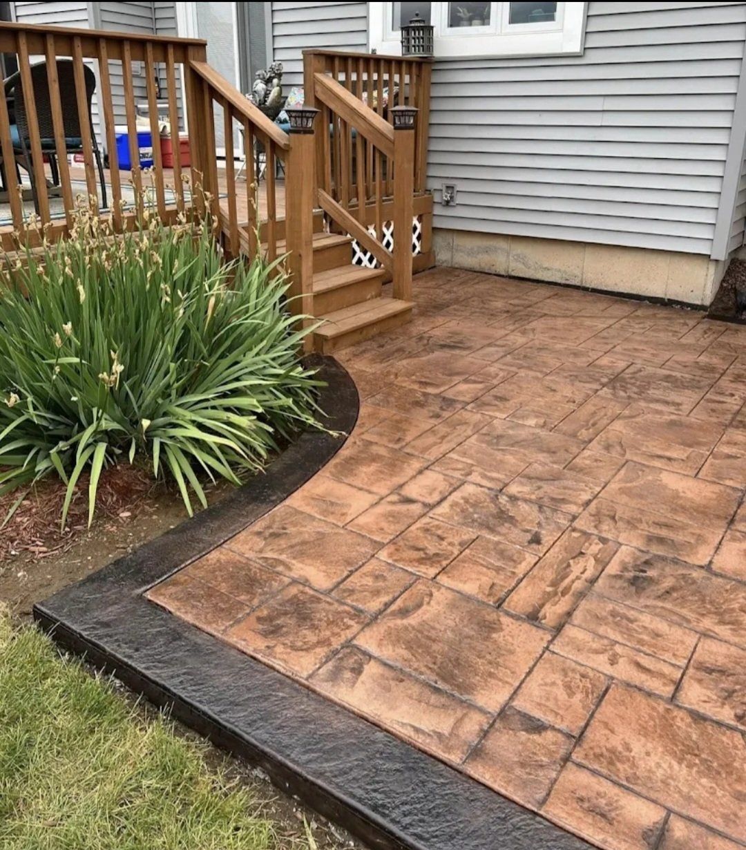 Brick patio beside wooden deck and stairs next to a house, with a small landscaped garden bed.