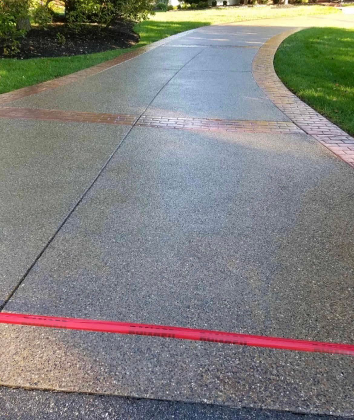Curved concrete driveway with a red line across it, bordered by grass and brick edging.